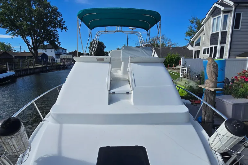Slide: The Image of 1995 Mainship 31 Sedan Bridge boat docked by waterfront homes, featuring a green canopy. - 10