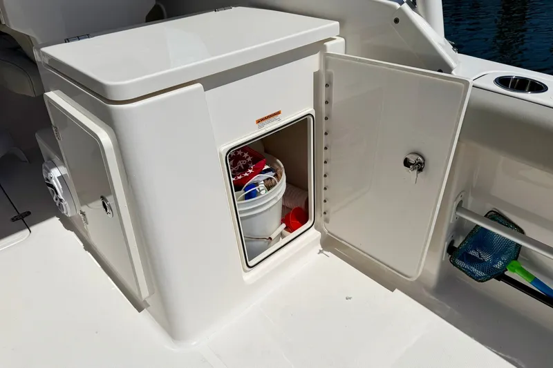 Slide: The Image of 2022 Pursuit DC 266 Dual Console boat storage compartment with open door and bucket inside. - 22