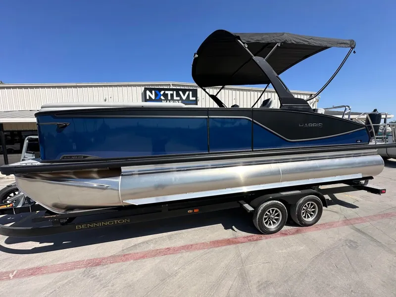 The Image of A 2027 Harris Sunliner 230 pontoon boat on a trailer, featuring a blue hull and black canopy. - 1