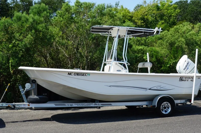 Slide: The Image of 2015 Carolina Skiff 218 DLV boat on trailer, surrounded by lush greenery. - 7