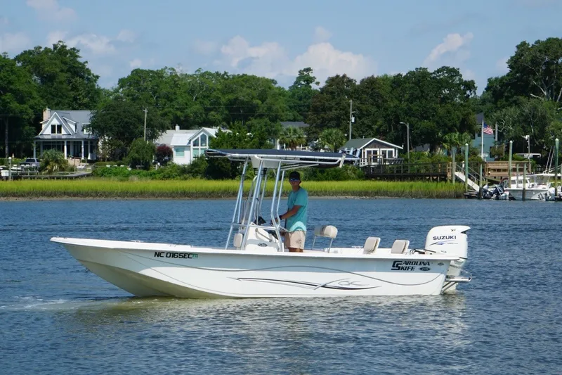 The Image of 2015 Carolina Skiff 218 DLV boat cruising on a scenic river with houses in the background. - 1