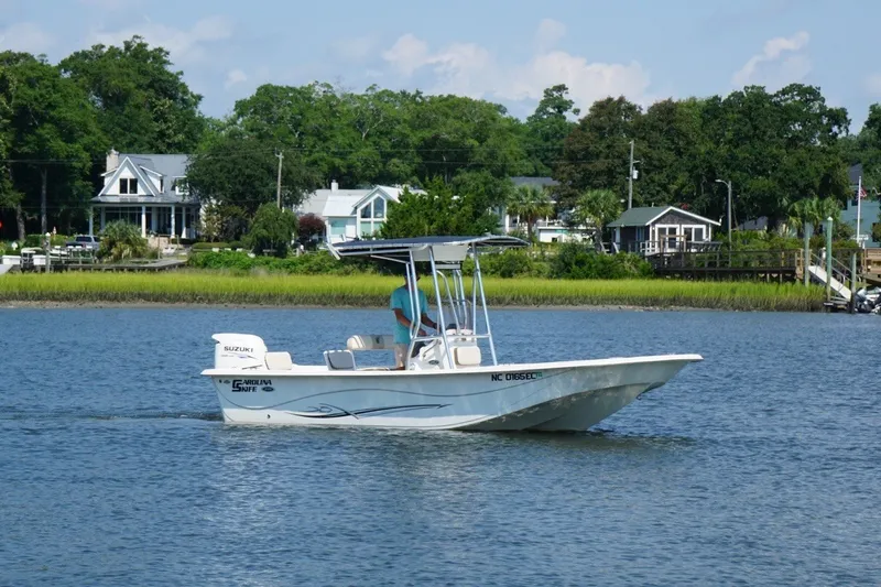 Slide: The Image of 2015 Carolina Skiff 218 DLV boat cruising on a scenic river near waterfront homes. - 2