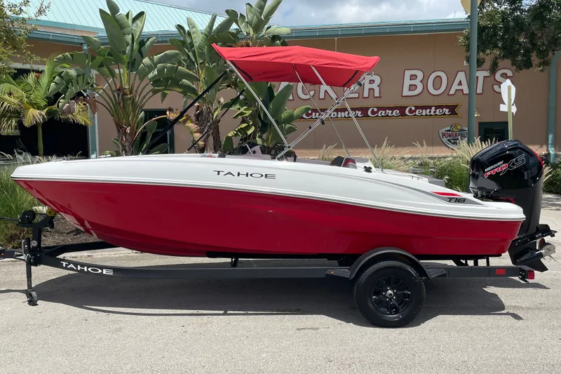 Slide: The Image of 2027 Tahoe T18 boat with red hull and canopy on trailer, parked outside a boat center. - 1