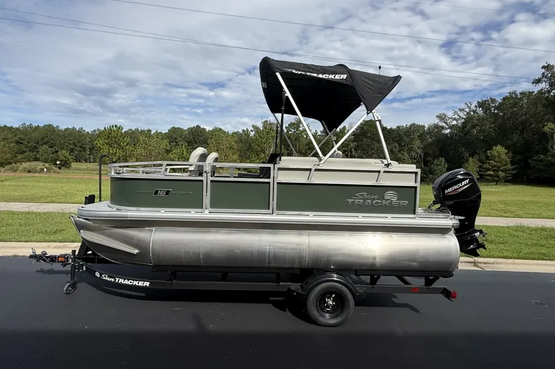 The Image of 2027 Sun Tracker Bass Buggy 16 XL Select pontoon boat on trailer, parked outdoors. - 0