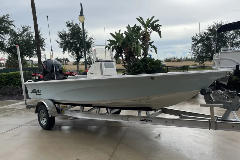 The Image of 2026 Mako 18 Pro Skiff boat on trailer, parked outdoors with trees in background. - 0