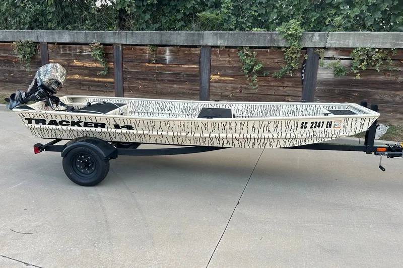 The Image of 2026 Tracker Grizzly 1436 boat on trailer, camouflage design, parked outdoors. - 0