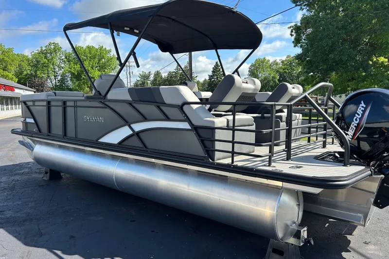 Slide: The Image of 2026 Sylvan L3 LZ Tritoon boat with Mercury engine, parked outdoors. - 24