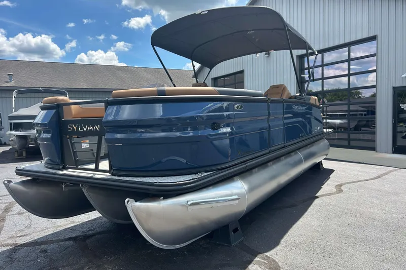 Slide: The Image of 2027 Sylvan X3 LZ DH Tritoon boat with canopy, parked outside a building. - 21
