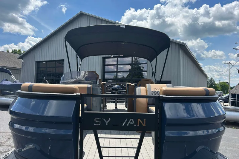 Slide: The Image of 2027 Sylvan X3 LZ DH Tritoon boat with canopy, parked outside a warehouse. - 22
