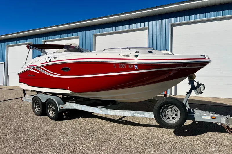 The Image of 2013 Hurricane SunDeck 2200 OB boat on trailer, red and white design, parked outdoors. - 0