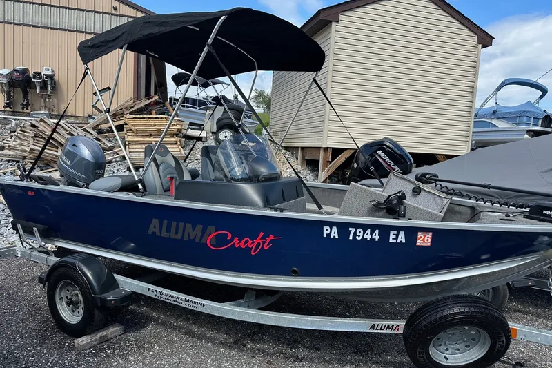 Slide: The Image of 2021 Alumacraft Classic 165 CS boat with canopy on trailer, parked near storage sheds. - 18