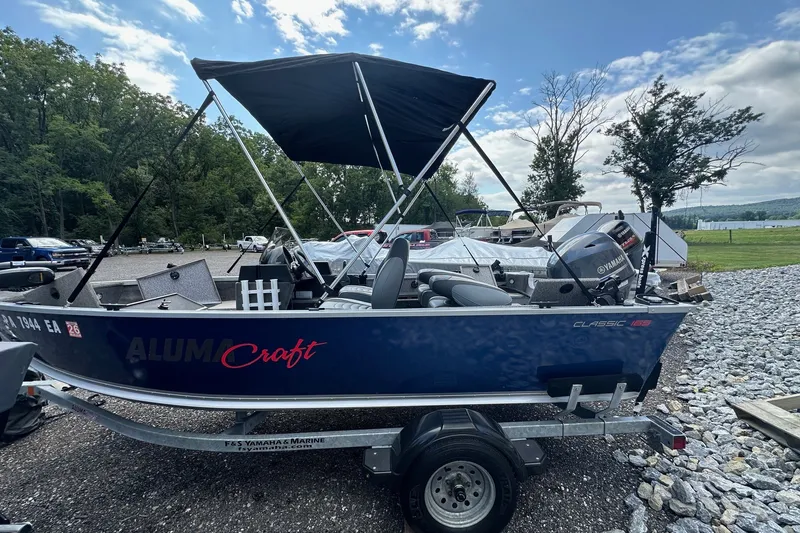 Slide: The Image of 2021 Alumacraft Classic 165 CS boat on trailer, parked outdoors under a blue sky. - 26