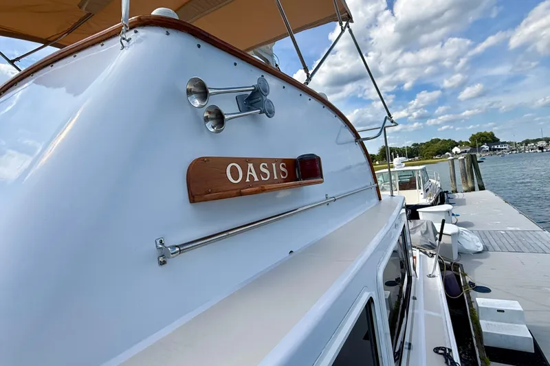 Slide: The Image of 1987 Wilbur Flybridge Cruiser "Oasis" docked by a scenic waterfront. - 29