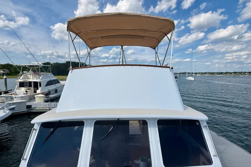Slide: The Image of 1987 Wilbur Flybridge Cruiser docked, featuring a tan canopy and scenic waterfront view. - 27