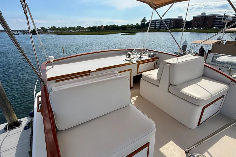 Slide: The Image of 1987 Wilbur Flybridge Cruiser with white seating, docked by a scenic waterfront. - 32