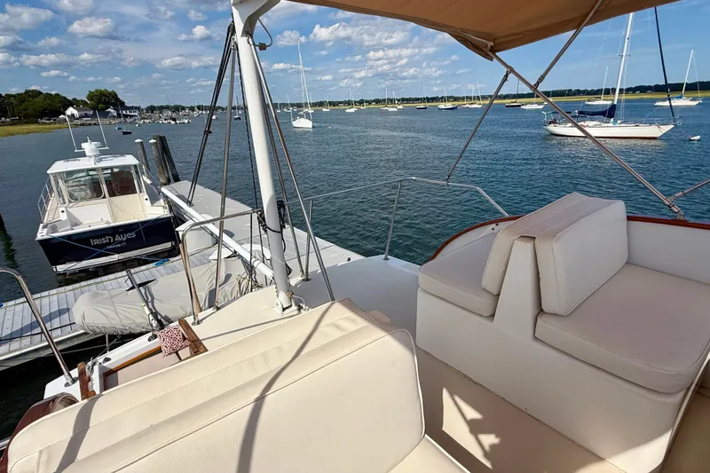 Slide: The Image of 1987 Wilbur Flybridge Cruiser docked, featuring spacious seating and scenic waterfront view. - 34