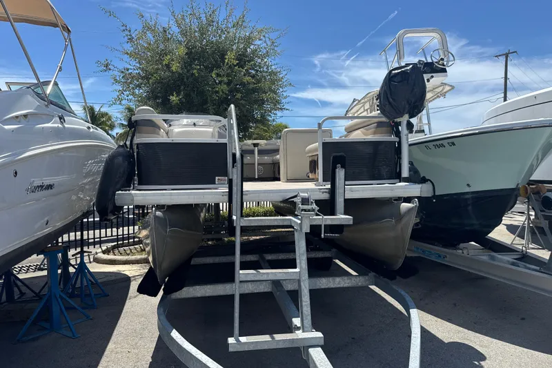 Slide: The Image of 2017 Godfrey Sweetwater Sunrise 22 pontoon boat on trailer, parked between other boats. - 1