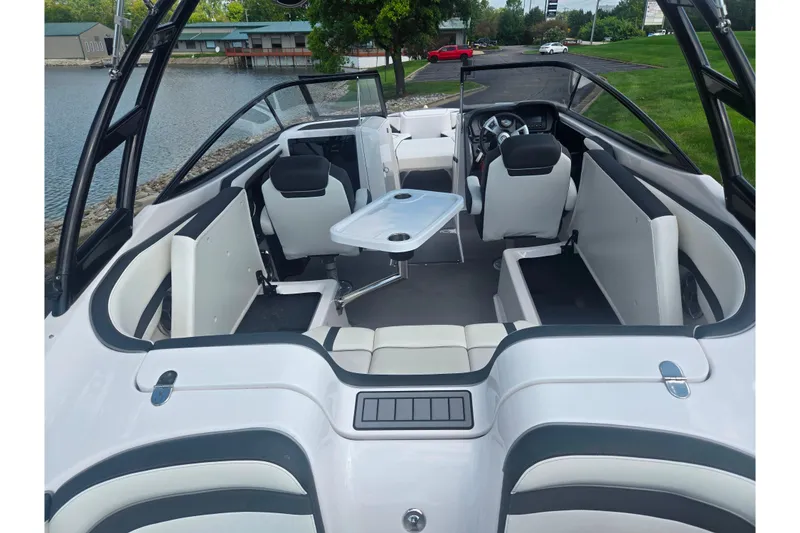 Slide: The Image of 2016 Yamaha Boats AR240 interior with seating and table, docked by a lake. - 11