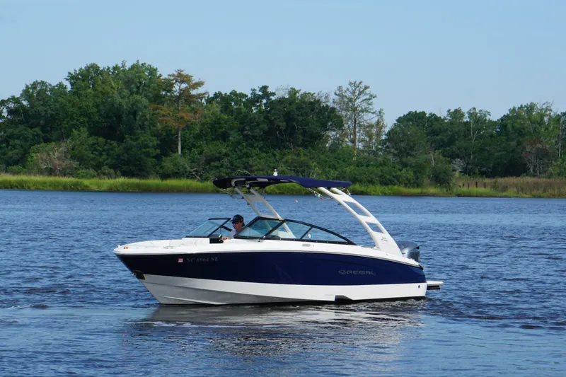 Slide: The Image of 2024 Regal LX2 boat cruising on a serene lake with lush green trees in the background. - 5