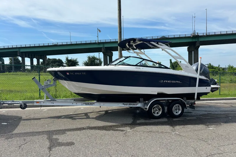 Slide: The Image of 2024 Regal LX2 boat on trailer, parked near a bridge, under a clear sky. - 10