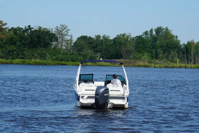Slide: The Image of 2024 Regal LX2 boat cruising on a serene lake with lush green shoreline. - 2