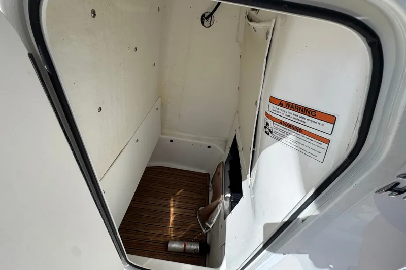 Slide: The Image of 2024 NauticStar 211 Hybrid storage compartment with warning label and wooden flooring. - 33