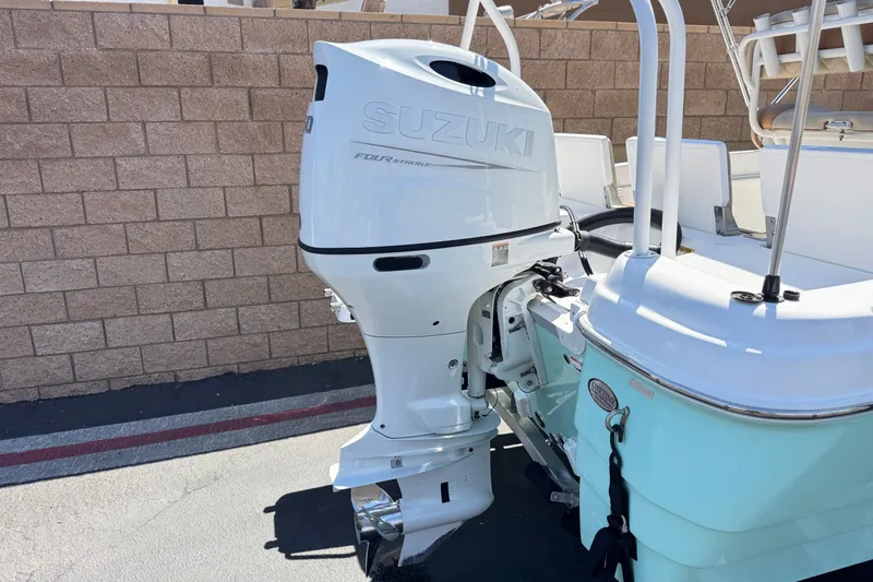 Slide: The Image of 2024 NauticStar 211 Hybrid boat with Suzuki outboard motor, parked near a brick wall. - 6