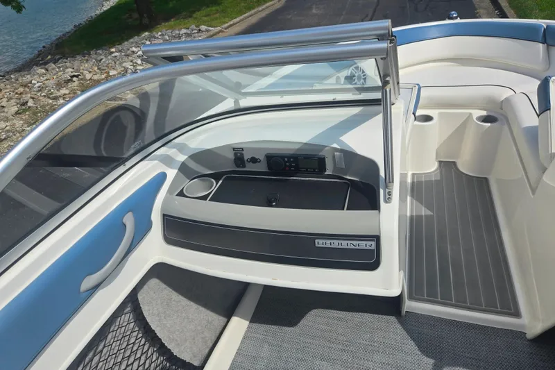 Slide: The Image of 2013 Bayliner 195 Bowrider interior with seating and dashboard, near a lakeside. - 13