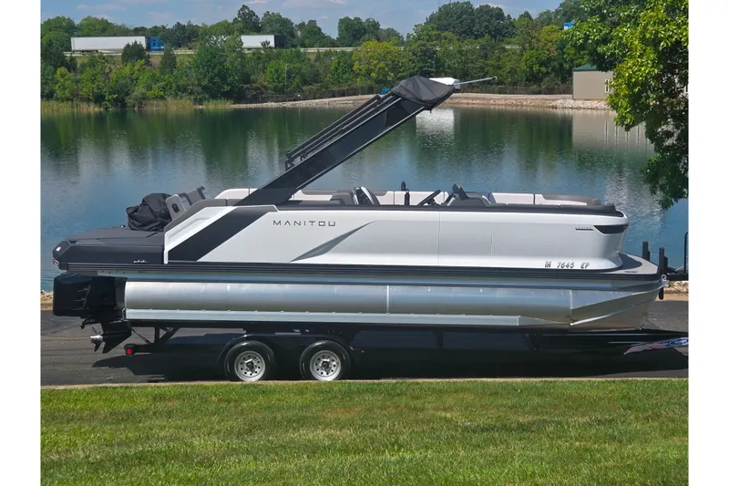 The Image of 2024 Manitou Cruise pontoon boat on trailer by a scenic lake. - 0