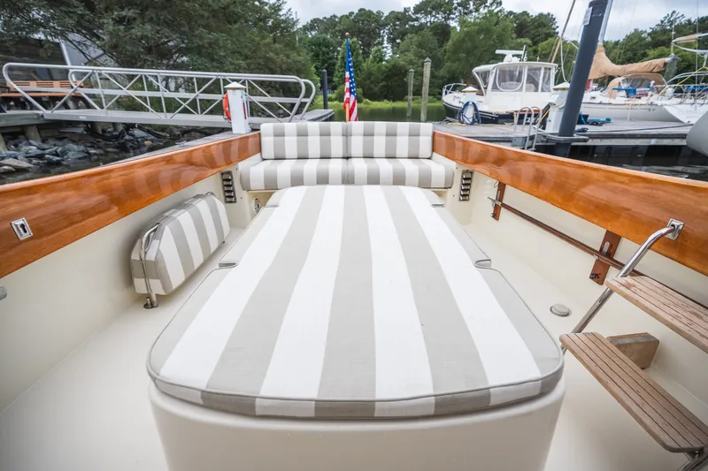 Slide: The Image of 2000 Hinckley Picnic Boat 36 Classic with striped seating, docked near lush greenery. - 42