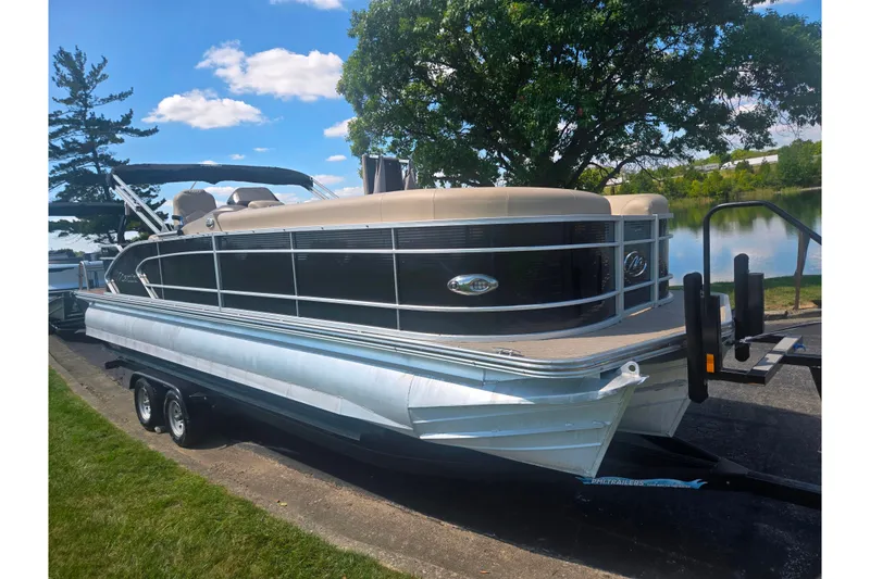 Slide: The Image of 2012 Manitou 25 Legacy pontoon boat on trailer by a lake, under a clear blue sky. - 8