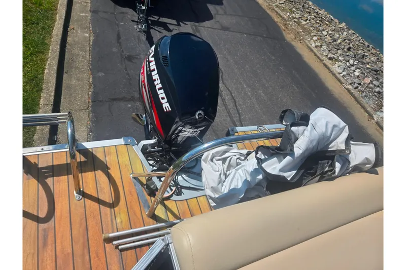 Slide: The Image of 2012 Manitou 25 Legacy boat with Evinrude motor, docked near a rocky shoreline. - 18