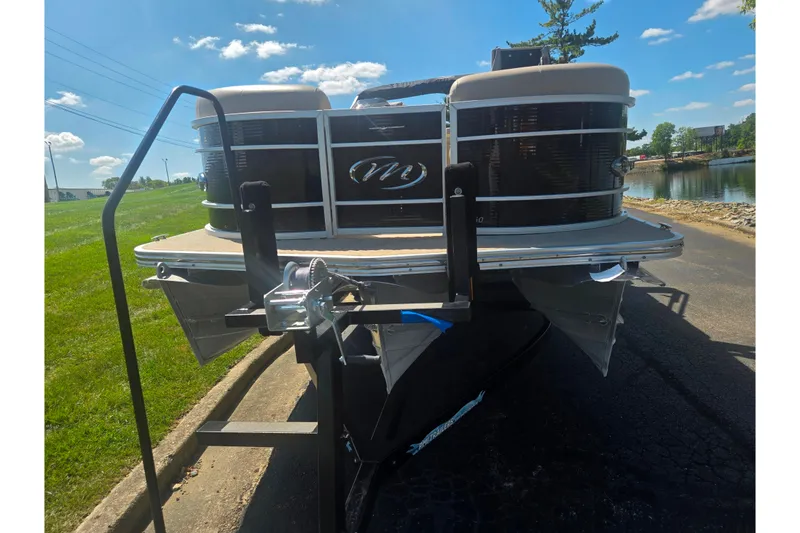 Slide: The Image of 2012 Manitou 25 Legacy pontoon boat on trailer, parked near a lake under a clear sky. - 6