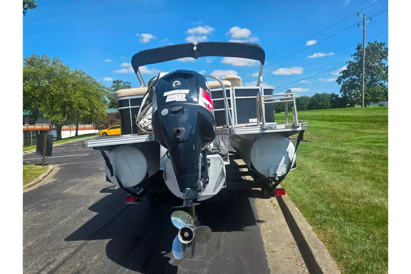 Slide: The Image of 2012 Manitou 25 Legacy pontoon boat with outboard motor, parked on a sunny day. - 2