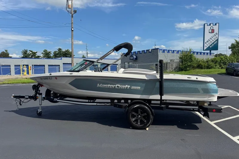 Slide: The Image of 2023 MasterCraft ProStar boat on trailer in parking lot, clear sky background. - 2