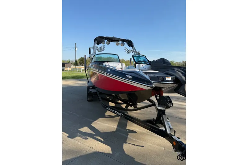 Slide: The Image of 2013 MasterCraft XStar boat on trailer, red and black design, parked outdoors. - 4