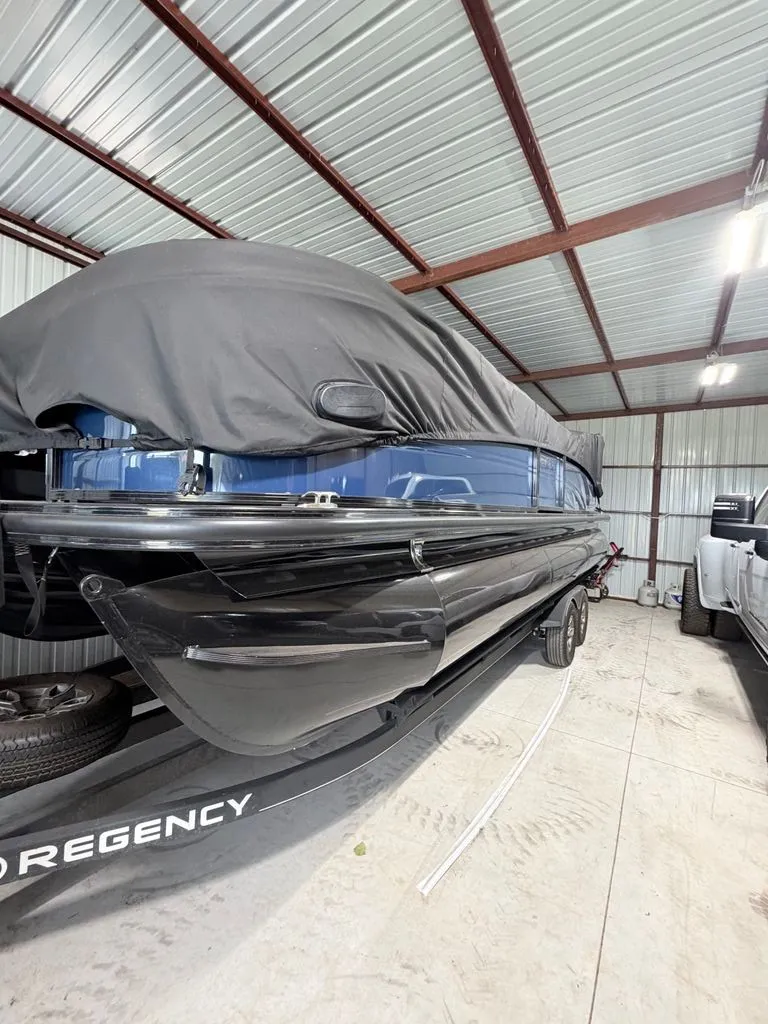 The Image of A 2025 Regency 230 LE3 pontoon boat in a storage facility, partially covered with a tarp. - 0
