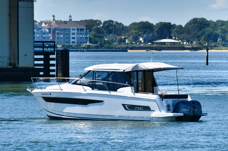 The Image of 2019 Jeanneau NC 895 boat on calm water near a bridge and shoreline. - 0