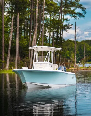 The Image of A 2027 Sea Hunt Ultra 229 boat on calm water, surrounded by trees. - 1
