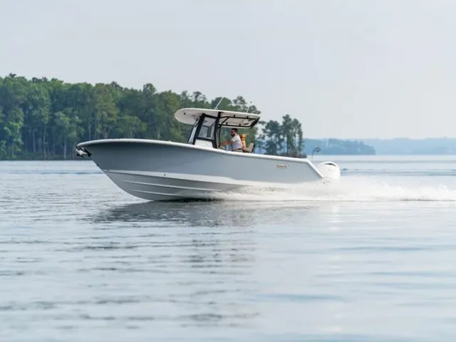 The Image of A 2027 Sea Hunt Gamefish 25 speeds across calm water, surrounded by trees. - 1