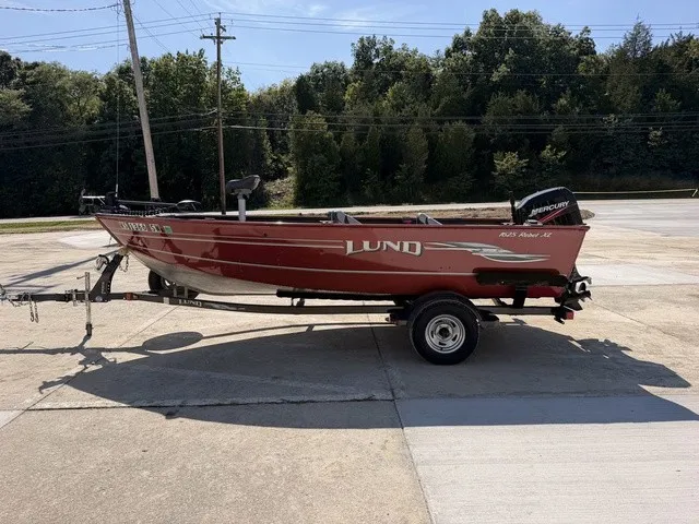 Slide: The Image of A red 2009 Lund 1625 Rebel XL boat on a trailer, parked on a concrete lot. - 15