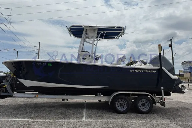 The Image of A 2013 Sportsman Heritage 211 Center Console boat on a trailer, featuring a blue hull and T-top. - 1