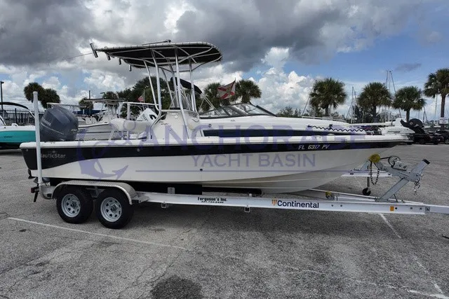 The Image of A 2015 NauticStar 210 Sport on a trailer, parked on a concrete lot with palm trees in the background. - 1