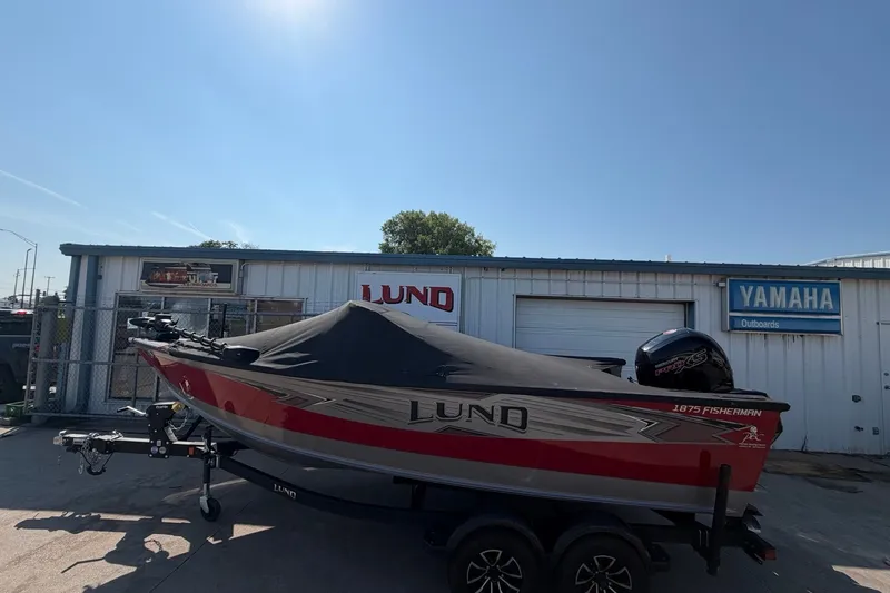 Slide: The Image of 2024 Lund 1875 Fisherman boat with cover, parked outside dealership under clear sky. - 5