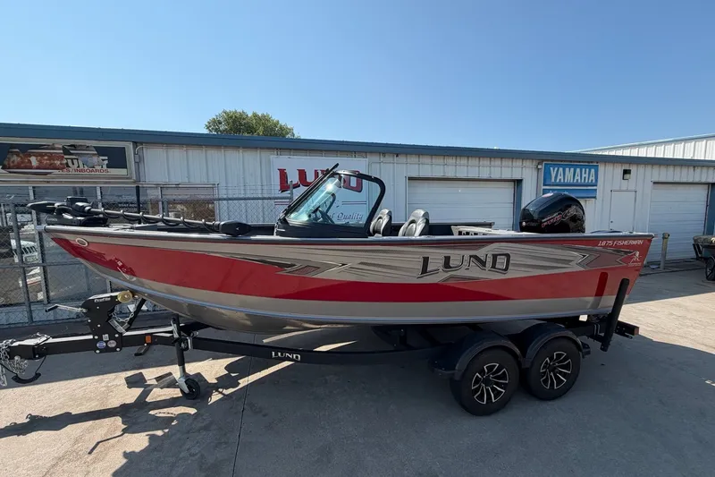 The Image of 2024 Lund 1875 Fisherman boat in red and silver, parked on a trailer outside dealership. - 0
