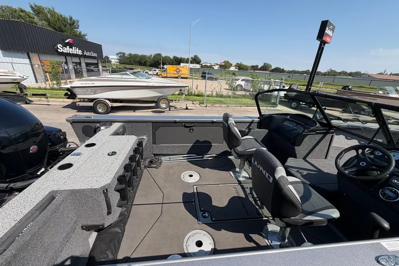 Slide: The Image of 2024 Lund 1875 Fisherman boat interior with seating and steering wheel, parked near Safelite AutoGlass. - 7