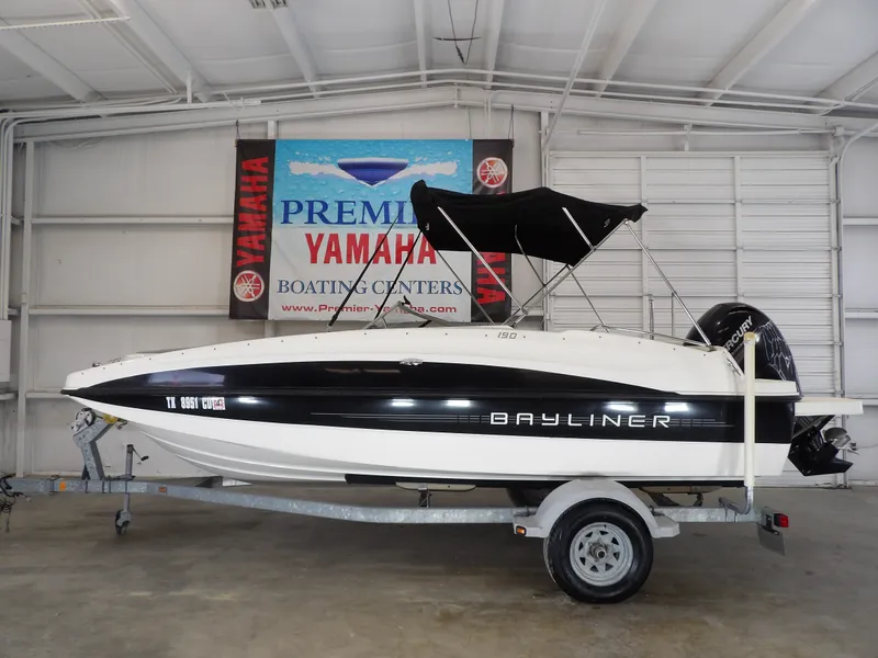 The Image of A 2013 Bayliner 190 Deck Boat on a trailer in a showroom setting. - 1