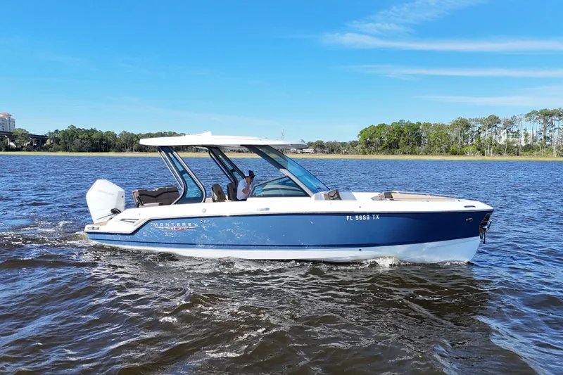 Slide: The Image of 2025 Monterey Elite 27 OB boat cruising on a scenic lake under a clear blue sky. - 2