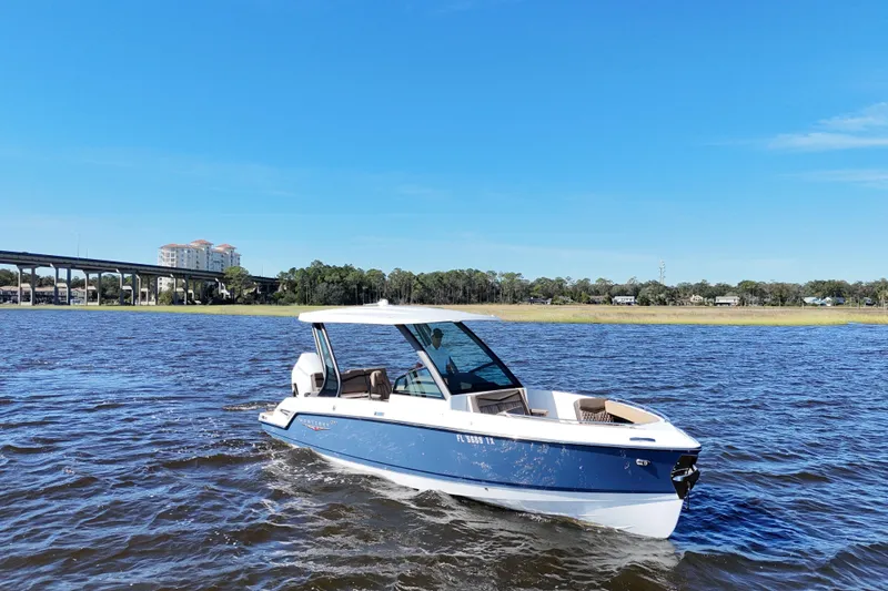 Slide: The Image of 2025 Monterey Elite 27 OB boat cruising on a sunny day, near a bridge and buildings. - 12