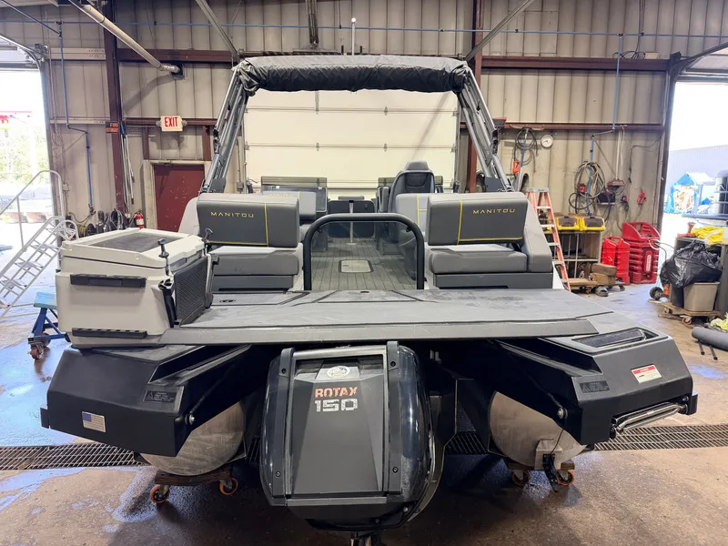 Slide: The Image of A 2023 Manitou 22 Explore Tritoon with a 150HP Rotax engine in a workshop. - 33